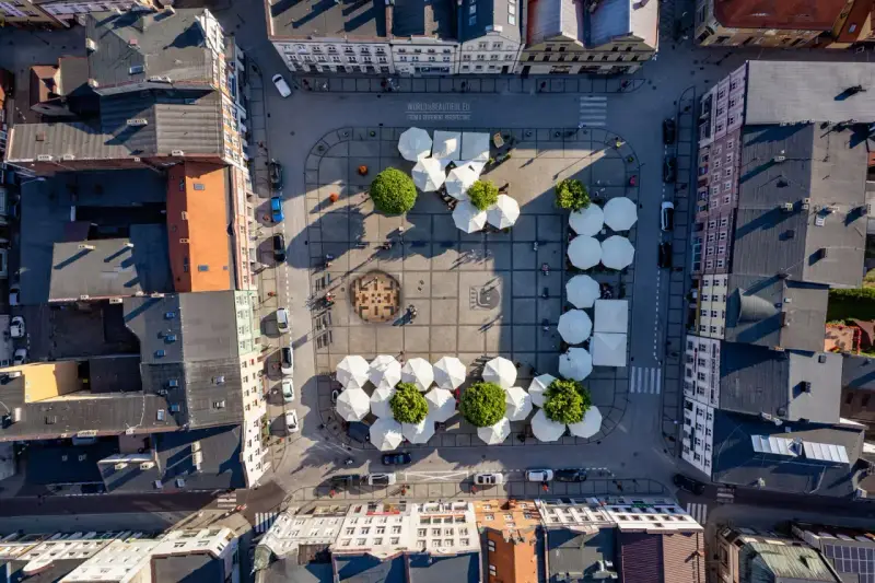 Widok z lotu ptaka na rynek w Kościerzynie, z białymi parasolami i zielenią.